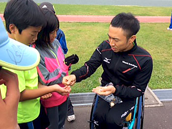 [写真]子供たちにリオパラリンピック記念コインを配る久保恒造選手