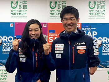 [写真]ワールドカップ札幌大会ポスターの前でガッツポーズの新田佳浩と阿部友里香