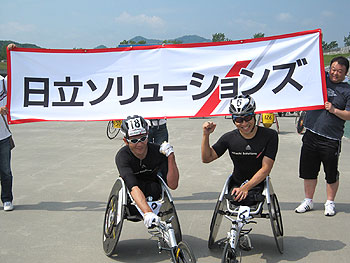 [写真]日立ソリューションズの横断幕の前で長田弘幸選手と久保恒造選手のガッツポーズ