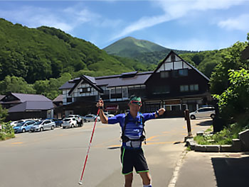 [写真]八甲田山を背景に両腕を上げて立つ新田佳浩