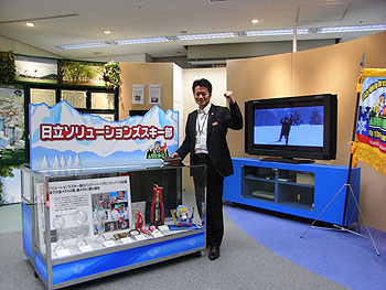 [写真]ショールームにてトロフィーやメダルなどの展示の前でガッツポーズする荒井秀樹監督